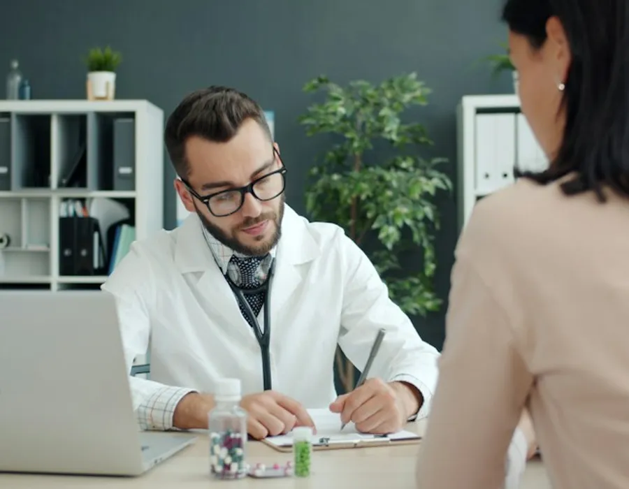 A doctor writing notes while a patient sits opposite