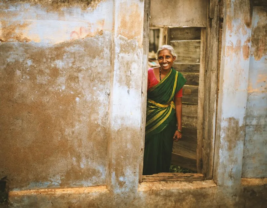 A smiling woman in a green sari standing in a doorway